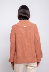 Sweater color crema de tejido trenzado con cuello alto, mangas largas abullonadas y detalle de flecos en el frente.