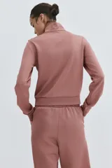Campera deportiva corta de punto grueso con leve brillo, color rosado, con cuello elevado, cierre frontal y bolsillos laterales insertados.
