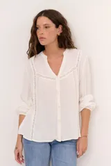 Camisa color natural de manga larga, con escote en V y detalles de encaje o calados decorativos en el frente y las mangas. Cierre frontal con botones.