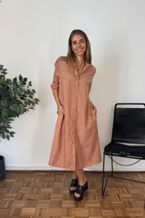 Vestido camisero largo color terracota/bronce, de manga larga con puños remangados, cuello solapa y cierre frontal de botones. Tiene un corte amplio y bolsillos laterales.