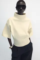 Jersey de punto color amarillo claro, con cuello subido, manga corta con hombreras y cintura entallada.