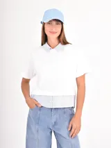 Remera de manga corta color blanco con cuello camisero y detalle de bajo en tela rayada azul y blanca, simulando una camisa debajo.