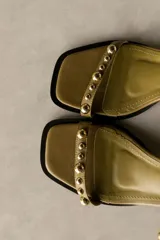 Sandalia de cuero color bronce metalizado, con punta cuadrada, taco ancho y bajo, y tiras finas adornadas con tachas esféricas plateadas.