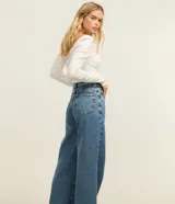 Pantalón wide leg de denim azul de talle alto con costuras pespunteadas en contraste. Cuenta con trabillas en la cintura, cierre de botón y cremallera, y bolsillos delanteros y traseros.