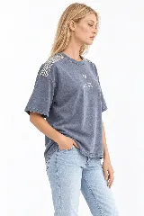 Remera oversize de algodón con acabado stonewash, color gris azulado, manga corta y cuello redondo. Cuenta con apliques bordados a mano en forma de hojas con canutillos plateados sobre los hombros.
