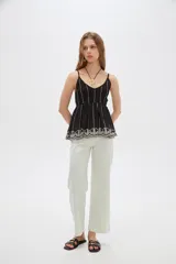Blusa de algodón negra con tirantes finos regulables, escote en V y diseño holgado. Presenta detalles de bordado en color blanco verticalmente en el pecho y un delicado diseño floral bordado en el ruedo.