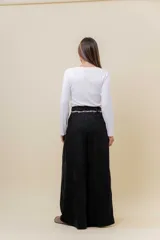 Pantalón wide leg de tiro alto en color negro, con diseño de pinzas delanteras que aportan volumen y caída fluida. Incluye bolsillos laterales y un lazo desmontable en la cintura que combina cordón con cinta de estampado animal print.