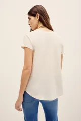 Remera básica de corte holgado, color negro, con mangas cortas y cuello redondo. Presenta un diseño con largo irregular y ruedo redondeado, confeccionada en algodón peruano con textura jaspeada.