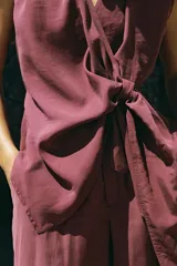 Top fluido sin mangas, de color bordó, con escote en V cruzado y detalle de nudo drapeado en el lateral delantero.