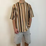 Remera de tejido de punto con diseño de rayas verticales en tonos tierra, negro y crema. Presenta un corte oversize con cuello redondo y mangas cortas.
