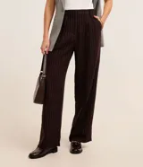 Pantalón de vestir de polivelour marrón con finas rayas verticales blancas, de corte recto y cintura alta, con cierre tradicional, pliegues y bolsillos.