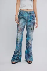 Jean de tiro medio y pierna flare de denim azul con estampa en toda la prenda y detalles de calados bordados florales en la parte inferior. Cuenta con cinco bolsillos y cierre frontal con cremallera.
