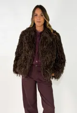 Chaqueta de textura peluda en color marrón, con diseño de flecos largos, cuello solapa y cierre frontal.