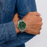 Reloj Casio de estilo deportivo con caja redonda de acero inoxidable y malla de eslabones plateada. Presenta una esfera verde con textura estriada, índices y manecillas luminiscentes, bisel giratorio unidireccional y ventana de calendario a las 4.