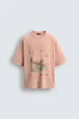 Camiseta de punto de algodón con corte boxy fit, cuello redondo y manga corta. Presenta un estampado frontal con diseño de paisaje y texto en tonos deslavados. La prenda tiene un efecto lavado que le da un aspecto envejecido e irregular.