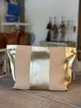 Cartera tipo sobre de cuero combinado en tonos beige y dorado, con tiras laterales con borlas colgantes.
