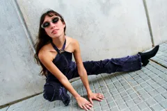 Top halter de denim con efecto lavado, corte entallado y escote alto. Presenta recortes frontales estructurados, terminación desflecada en el frente y un aplique metálico decorativo en el centro del cuello.