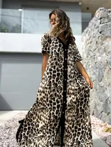 Vestido largo de corte holgado con estampado animal print de leopardo. Presenta una botonadura frontal completa sobre una franja vertical de color negro que recorre el centro de la prenda, cuello en V y mangas cortas.