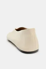 Zapato plano tipo bailarina en piel color beige, con efecto soft y pespuntes en la parte frontal. Presenta escote en pico con detalle metálico y acabado en punta redonda.