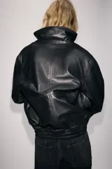 Cazadora de piel 100% color negro de Zara Woman Collection, con cuello subido, manga larga y bolsillos de plastrón con solapa en el delantero. Cuenta con bajo elástico y cierre frontal con cremallera y botones a presión ocultos.