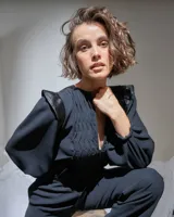 Mono largo negro de acetato con mangas largas abullonadas con elástico en los puños, detalle de raso en hombros y cinturón, escote en V regulable con cierre invisible y textura plisada artesanal en el frente superior.