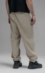 Pantalón deportivo de microfibra color beige, con corte regular y diseño de inspiración vintage. Presenta vivos laterales a contratono, cintura elástica y puños elásticos en los tobillos.