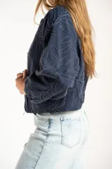 Campera tipo bomber color azul, con cierre frontal y diseño de bordado floral en toda la prenda. Presenta puños y ruedo con elástico, y un corte holgado.