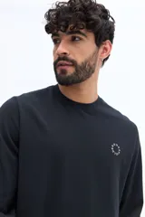 Remera de manga larga color blanco roto o gris muy claro, con escote redondo y un pequeño logo circular estampado en el pecho.