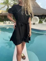 Vestido corto blanco de lino con corte evasé, mangas cortas con volados y cinto del mismo material.