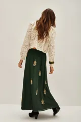 Vestido largo de satén color verde oscuro, con mangas tres cuartos terminadas en volados. Presenta un diseño con bordados dorados detallados en el pecho y cuello, además de motivos florales bordados dispersos a lo largo de la falda. Incluye un cinturón fino con aplicaciones brillantes.