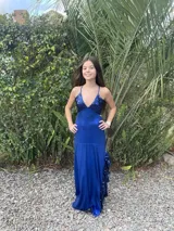 Vestido largo de satén color marrón con acabado metalizado, escote en V, tirantes finos cruzados en la espalda y diseño con corte bajo el busto y volados en la falda.