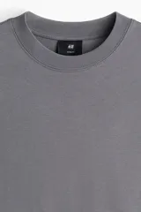 Remera de manga larga color gris oscuro, confeccionada en punto de algodón de peso medio. Presenta cuello redondo acanalado, hombros caídos, puños acanalados y bajo recto. Tiene un corte holgado.