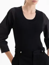 Top de tejido de punto acanalado en color blanco, con cuello redondo y mangas tres cuartos de tela plana con volumen. Presenta un diseño ajustado al cuerpo que contrasta con la estructura de las mangas.