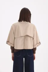 Piloto corto estilo camisa en color beige, con cuello clásico, cierre frontal de botones y mangas anchas con detalle de trabas en los puños.