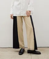 Pantalón de corte recto y tiro alto, confeccionado en algodón con diseño bicolor que combina paneles laterales en negro y panel central en beige, unidos por costuras visibles a contratono.