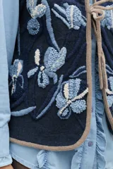 Chaleco de lana color rosa con bordados florales artesanales en tonos rosados y marrones. Presenta un diseño sin mangas con cierre frontal mediante lazos ajustables y terminaciones en color marrón.