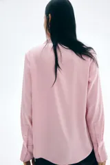 Blusa de manga larga color rosado pálido con acabado satinado. Presenta cuello clásico, escote en V con cierre de botones frontales y puños anchos.
