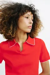 Top de punto color crudo, con cuello polo y escote en V. Cuenta con mangas cortas y detalle de puntilla con forma de onda en el cuello y los puños.