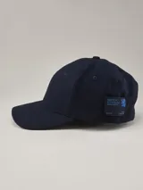 Gorra de béisbol de paño en color azul marino, con etiqueta lateral con logo de la marca.