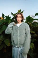 Campera con capucha de tejido de punto acanalado en color verde, con cierre frontal completo, bolsillos tipo canguro y detalles de efecto desgastado en los bordes.