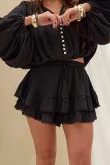 Short pollera negro de tiro alto, confeccionado en tejido texturizado con cintura elástica ajustable mediante cordón, diseño de doble volado y detalles de encaje en los bordes.