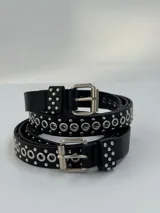 Cinto fino de cuero negro con hebilla metálica plateada y ojales metálicos plateados.