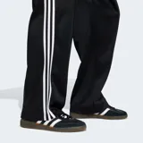 Pantalón deportivo Adidas Originals de corte holgado, color negro con las icónicas tres tiras blancas laterales y logo del trifolio bordado en la pierna.
