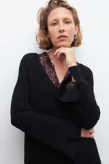 Sweater negro de tejido de punto grueso, con escote en V y detalle de cinta estampada floral en el borde del escote.