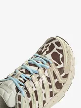 Championes Adidas Adistar Control 5 con diseño de estampado animal print tipo vaca en tonos marrón y blanco. Presenta detalles en color beige, acentos en celeste en los cordones y la entresuela, y estructura reforzada con paneles laterales.