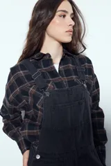 Enterito de denim negro con calce relajado y silueta amplia, inspirado en la estética workwear. Presenta tiradores regulables, pechera con bolsillo frontal y bolsillos laterales funcionales.