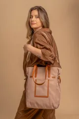 Bolso tipo tote bag de símil cuero color rosa pálido, con asas dobles y detalles de costura en color beige claro. Presenta un bolsillo frontal rectangular aplicado y herrajes metálicos.