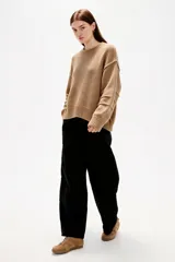 Sweater de punto canalé color beige, de corte holgado, con cuello redondo a la base y mangas largas con costuras decorativas.