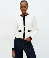 Cardigan de punto color blanco con detalles en negro en cuello, puños y tapeta frontal. Presenta cierre frontal con botones perlados y dos bolsillos delanteros falsos con solapa bicolor.
