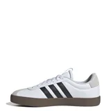 Championes urbanos Adidas modelo VL Court 3.0, con parte superior de cuero sintético blanco, icónicas tres tiras laterales en negro y puntera de gamuza gris. Presenta una suela de caucho vulcanizada en color marrón y cierre de cordones.